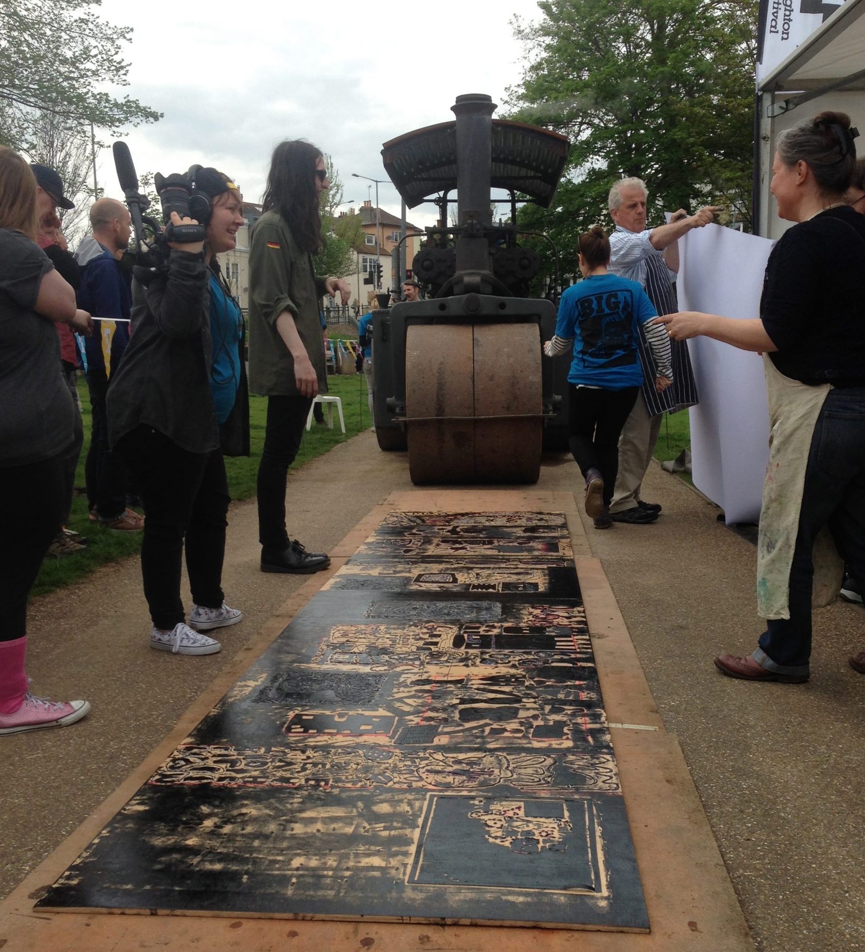 Art students and learning disabled artists print a large collograph using a steamroller at the Big Steam Print fair, at the Level, Brighton